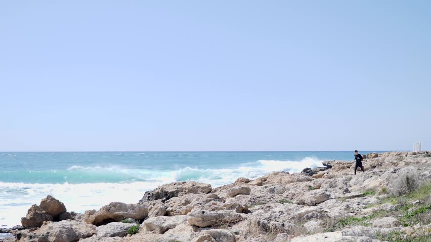 Caucasian athletic man running over the rocks on a rocky beach wearing black outfit. Slow motion