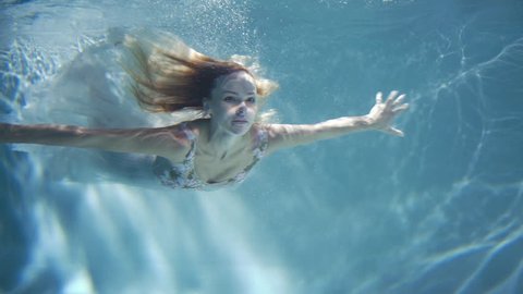 A woman in a white dress as a mermaid swimming under water.