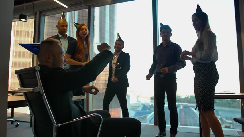 Happy employees celebrating birthday at the office with serpentine. Good relationships with top-brass. Daylight, smiles and dancing in holiday caps.
