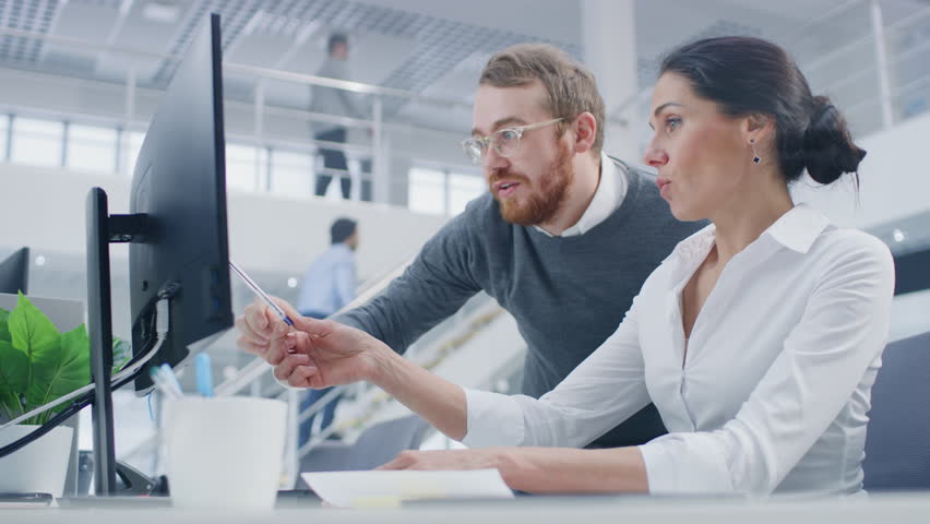 Beautiful Businesswoman Uses Desktop Computer, Consults Her Project Manager about Documents with Graphs and Statistics. In the Background Big Corporate Firm Office Royalty-Free Stock Footage #1027449083
