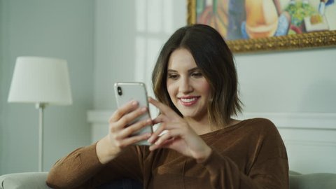 Close up of smiling woman sitting on sofa reading social media on cell phone / Cedar Hills, Utah, United States