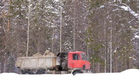 Dirty truck with ore rides on a winter forest road. Slow motion.