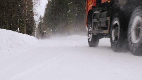 Two industrial trucks move along a winter forest road. Slow motion.