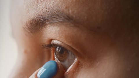 A beautiful young girl puts contact lenses in her eye close-up, macro. Blinking distributes the lens in the pupil. Brown eyes, black eyelashes, transparent lenses. Slow motion, 4K