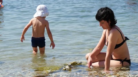 A child and his mother play on the sea beach with pebbles. The concept of a happy family and family vacation