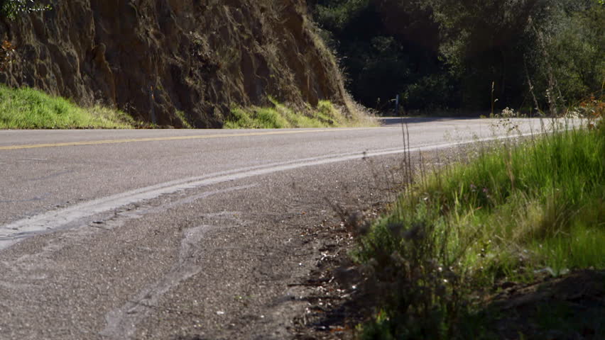 A person riding a motorcycle wearing full red protective gear on a mountain road in the desert of California.