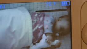 A baby monitor shows a baby girl in a crib playing with her toys