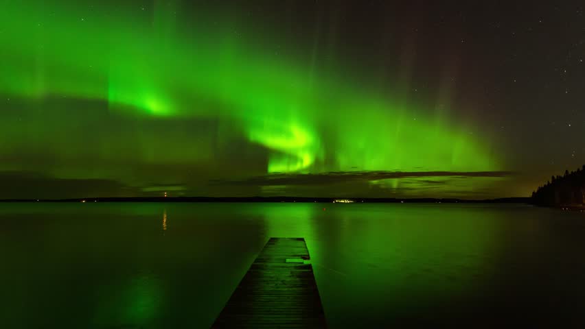 Epic time lapse of auroras above lake - Dock leading into the scene. Stars shining, clouds at horizon. In Tampere, Finland.