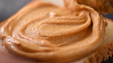 Peanut butter. Person making sandwiches with Creamy smooth peanut butter. Bread and peanut butter on a table. Natural nutrition and organic food. American cuisine. 4K UHD video, slow motion