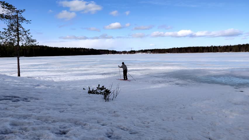 Single woman skiing in the frozen lake under the blue sky and white cloud in a sunny windy day 4K footage