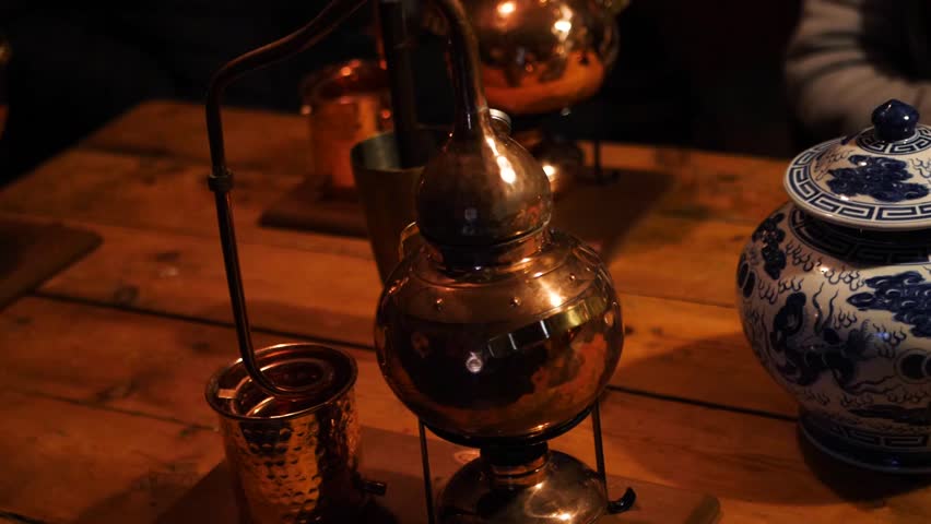 Sliding shot of a vintage, metal, small gin distillery kit, on a wooden table in a dark room
