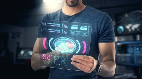 Independent and Young Male Robotic Design Engineer and Entrepreneur uses a Modern Transparent Holographic Touchscreen Tablet in an Underground Hi-Tech Laboratory. Modern Glass.
