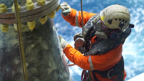 An abseiler complete with personal protective equipment (PPE) standing of the vessel at the edge of oil and gas rig platform for touch up painting activities.