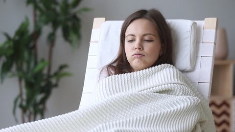 Young woman sitting on rocking chair covered with plaid shiver freeze feeling cold at home with no central heating problem in chill season, sick ill girl wrapped in blanket having fever flu symptoms
