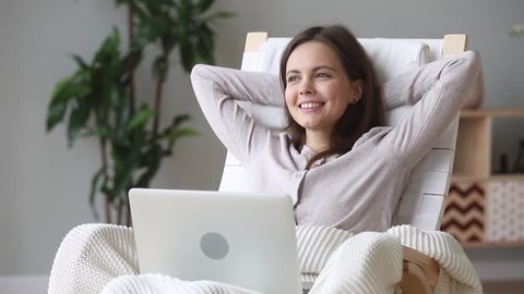 Dreamy relaxed teen girl sitting in rocking chair resting at home with laptop thinking dreaming enjoy stress free day, inspired young woman relaxing hands behind head holding computer dreaming