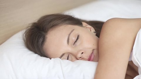 Calm young woman sleeping well in comfortable cozy fresh bed on soft pillow white linen orthopedic mattress, peaceful serene girl resting lying asleep enjoying healthy good sleep nap in the morning