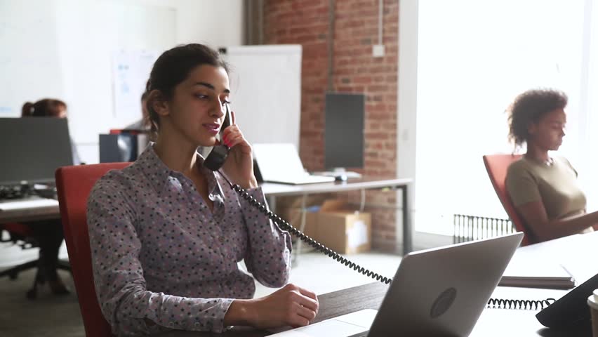 Young indian businesswoman talking on the phone consulting client in corporate office, focused hindu sales manager worker sitting at work desk with laptop making telephone call selling services Royalty-Free Stock Footage #1027488398