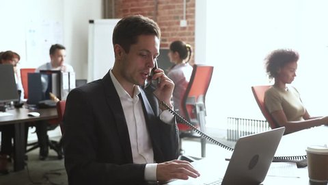 Male broker sales manager worker in suit talking on the phone using laptop at work desk, serious businessman employee making telephone call consulting customer in modern office at corporate workplace