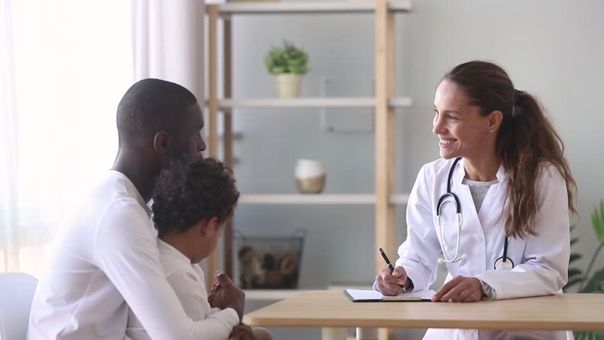 Young female caucasian doctor make notes listen to african american father of little ill child son patient tell complaints, black dad with kid boy visit pediatrician talk at appointment consultation | Shutterstock HD Video #1027488416