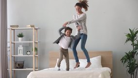 Happy family african american multiracial kid boy and caucasian mom baby sitter holding hands jumping on bed young mother having fun laughing playing funny active game with cute child son in bedroom - Powered by Shutterstock - Get 15% off with code: PIKWIZARD15