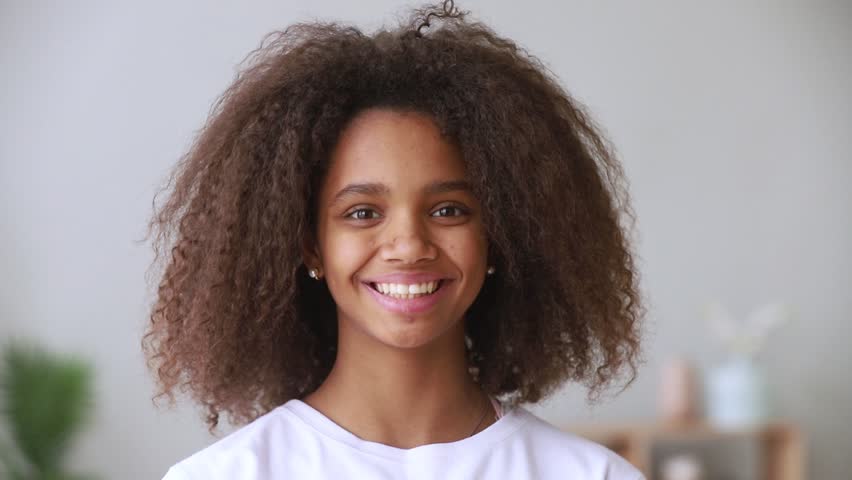 Pretty african american teen school girl looking at camera, adolescent funny mixed race teenage model with afro hair and beautiful face toothy smile posing at home, happy black teenager, portrait Royalty-Free Stock Footage #1027488545