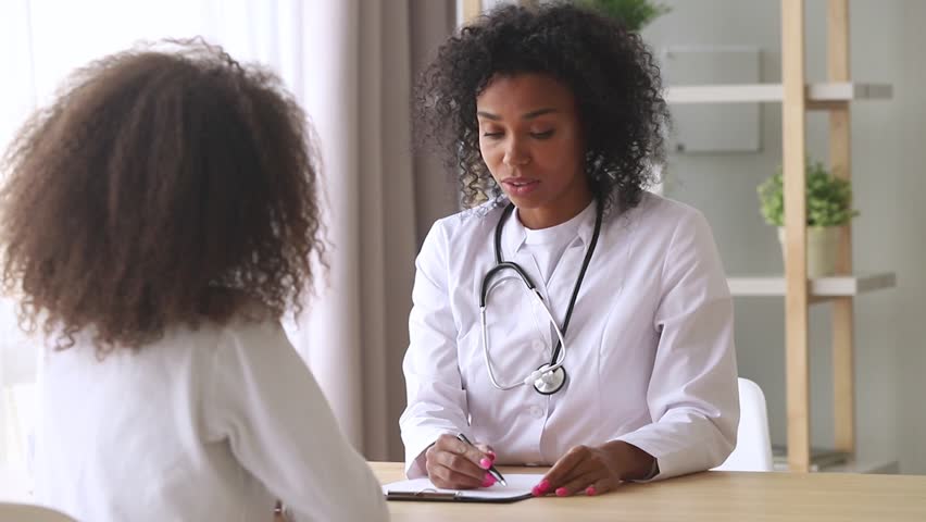 Young african american female doctor pediatrician talking to teen girl patient making notes in clipboard card explaining health care to black school teenager fill form at medical checkup appointment | Shutterstock HD Video #1027488548