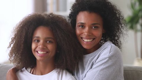 Happy african american family mom with teen daughter hugging laughing looking at camera, cheerful black mother embracing child teenage girl cuddling having fun feeling love and bonding, portrait