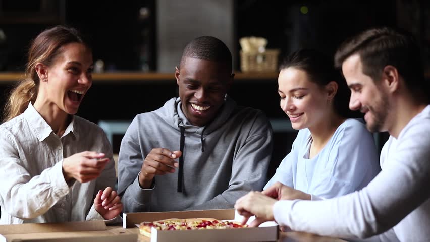 Multicultural happy friends talking laughing sharing takeaway pizza meal together in cafe indoors, smiling diverse young mates students having fun eating food together at meeting sitting at table Royalty-Free Stock Footage #1027488611