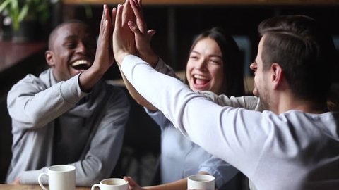 Diverse young happy friends join hands giving high five together celebrating multicultural friendship at reunion cafe meeting, multiracial mates students team bonding engaged in unity support concept