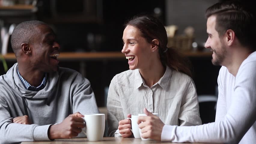Happy diverse young friends chatting laughing at coffeehouse meeting, multicultural cheerful people group talking sit at cafe table drink coffee tea together, multi-ethnic friendship and fun concept | Shutterstock HD Video #1027488629
