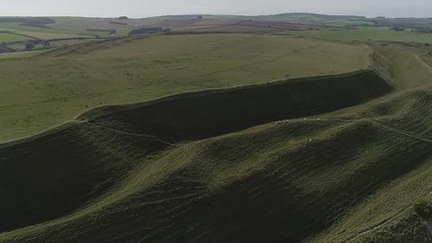 Aerial tracking along the northern side of the iron age hill fort known as Maiden Castle. Three levels of earthworks can be seen. Dorchester, Dorset. Cropped