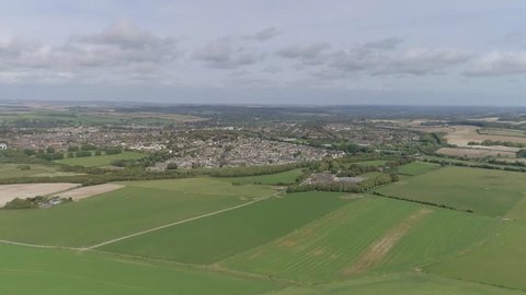 Wide aerial tracking forward toward the town of Poundbury, just outside of Dorchester, Summer weather, fields are vibrant. Amazing view with Dorset countryside surrounding in every direction.