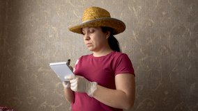 A woman makes a note in a notebook. On his head a straw hat. Preparation for work. Burgundy t-shirt. Gray Wallpaper on the wall. Home-room. A doctor, a vet, a gardener, a villager. 4K video.