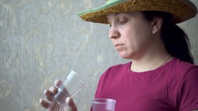Woman examines plastic cups. On his head a straw hat. Burgundy t-shirt. Gray Wallpaper on the wall. Home-room. A doctor, a vet, a gardener, a villager. 4K video.
