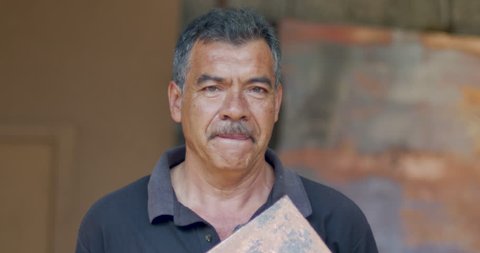 Portrait of a serious looking hispanic man holding a piece of patina copper while looking at the camera