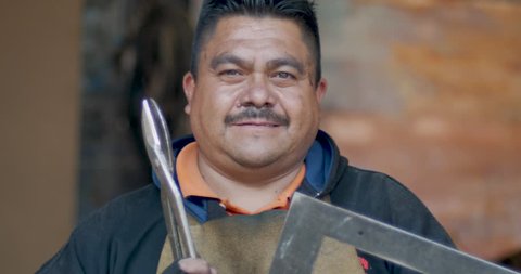 Portrait of a serious Hispanic man looking at the camera holding scissors and a ruler in his metal shop