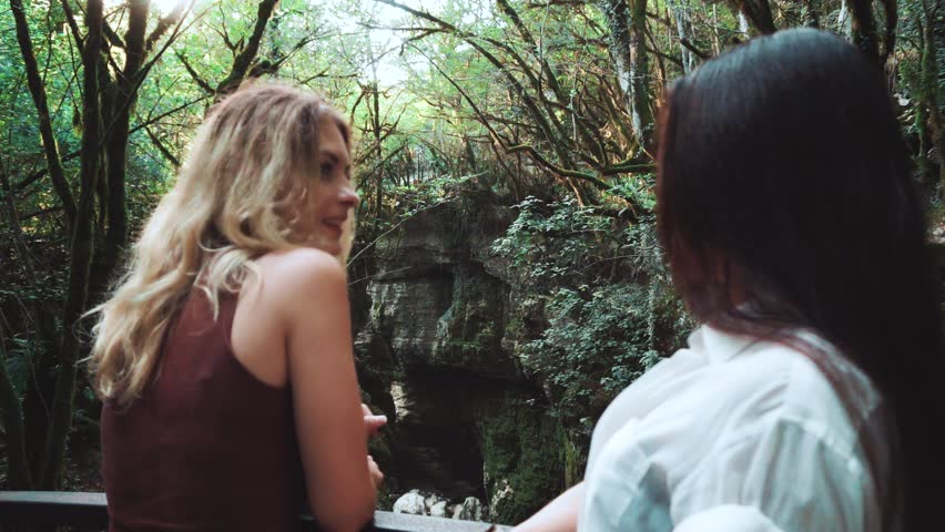 two pretty white ladies standing fence bridge over Martvili canyon  Georgia, young women admire beauty wildlife, brunette blonde friend holiday vacation young pepple foreign country budget relax trip 
