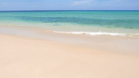 Wide shot of gentle waves on a tropical white sand beach with clear turquoise water.