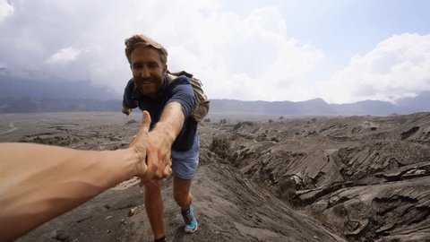 Young man hiking, pulls out hand to reach the one of teammate. A helping hand to reach the top of crater volcano. Bromo volcano region in Indonesia, Asia 