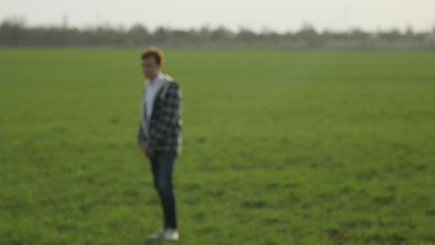 handsome boy walking in the green grass field at sunset