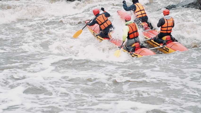 Rafting team descending raging rapids in mountain river with paddles splashing in water in slow motion. Close-up