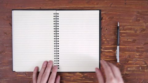 Man's hands turning over clean blank pages from recycled paper in big notebook, isolated on white wooden table , then closing it.