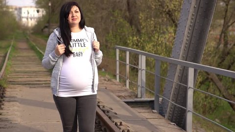 Young pregnant woman walks along a railway bridge in the forest. Happy pregnant woman is thinking about future motherhood. Woman at 36 weeks gestation (9 month).