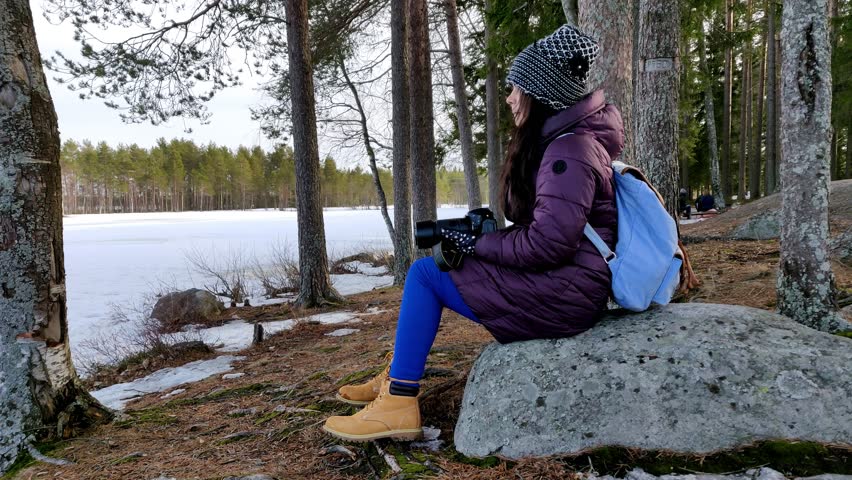 Thoughtful beautiful woman taking pictures in outdoor snow covered nature in a cold windy day in fast motion