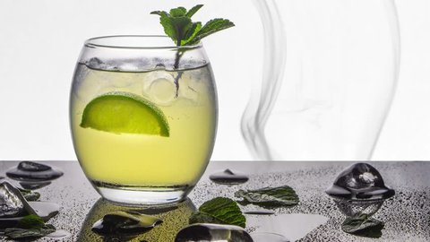 An oval glass of mojito summer cocktail or punch with fresh organic lime and mint on a black stone base scattered with ice and a smoke background