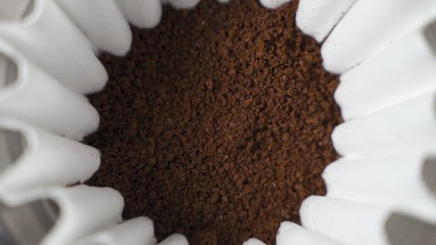 Hot water pour over into ground coffee beans close up slow motion