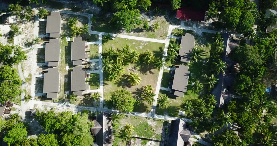 Drone shot of tropical, green island-resort with bungalows and green palms in hot sunny day.