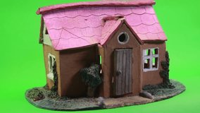 Small Ceramic House with Red Roof On Green Background.