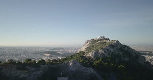 Forward aerial drone view approaching from side of Mount Lycabettus flying next to St. George Chapel to reveal the Acropolis and cityscape of Athens, Greece
