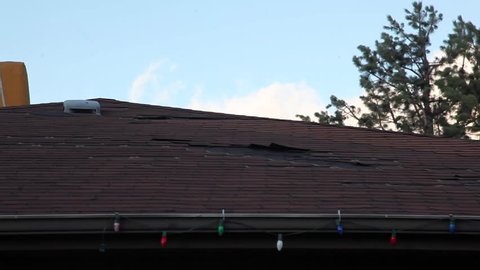 Shingles getting blown off of a roof in the middle of some strong winds.